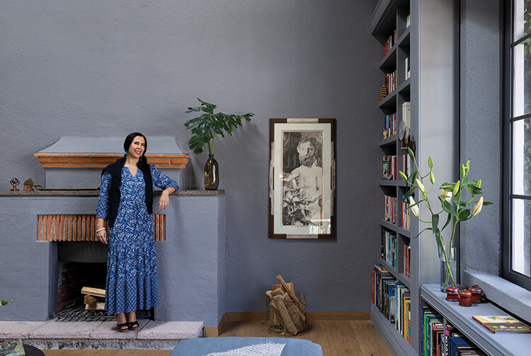 Mariangel Coghlan en un espacio interior sereno junto a una chimenea y biblioteca.